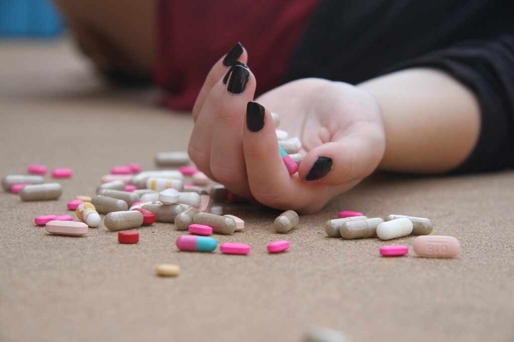 Mano de persona acostada sostiene muchas pastillas simulando tentativa de suicidio